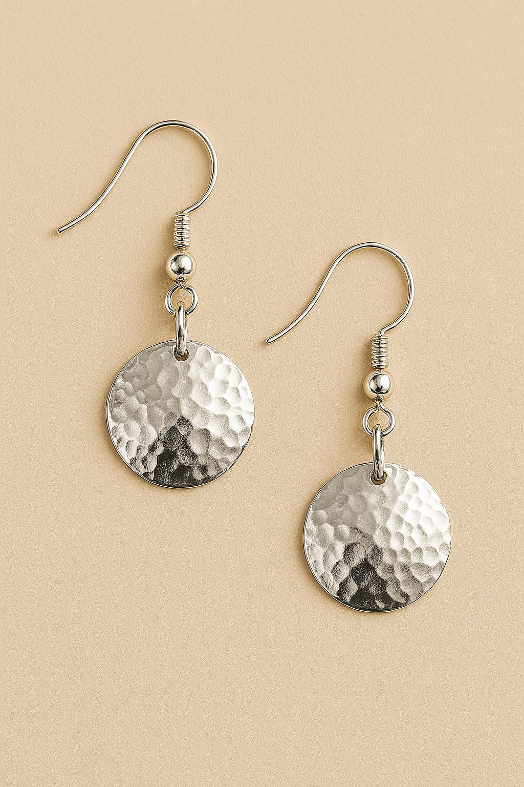 Pair of silver hammered disc earrings on a beige background