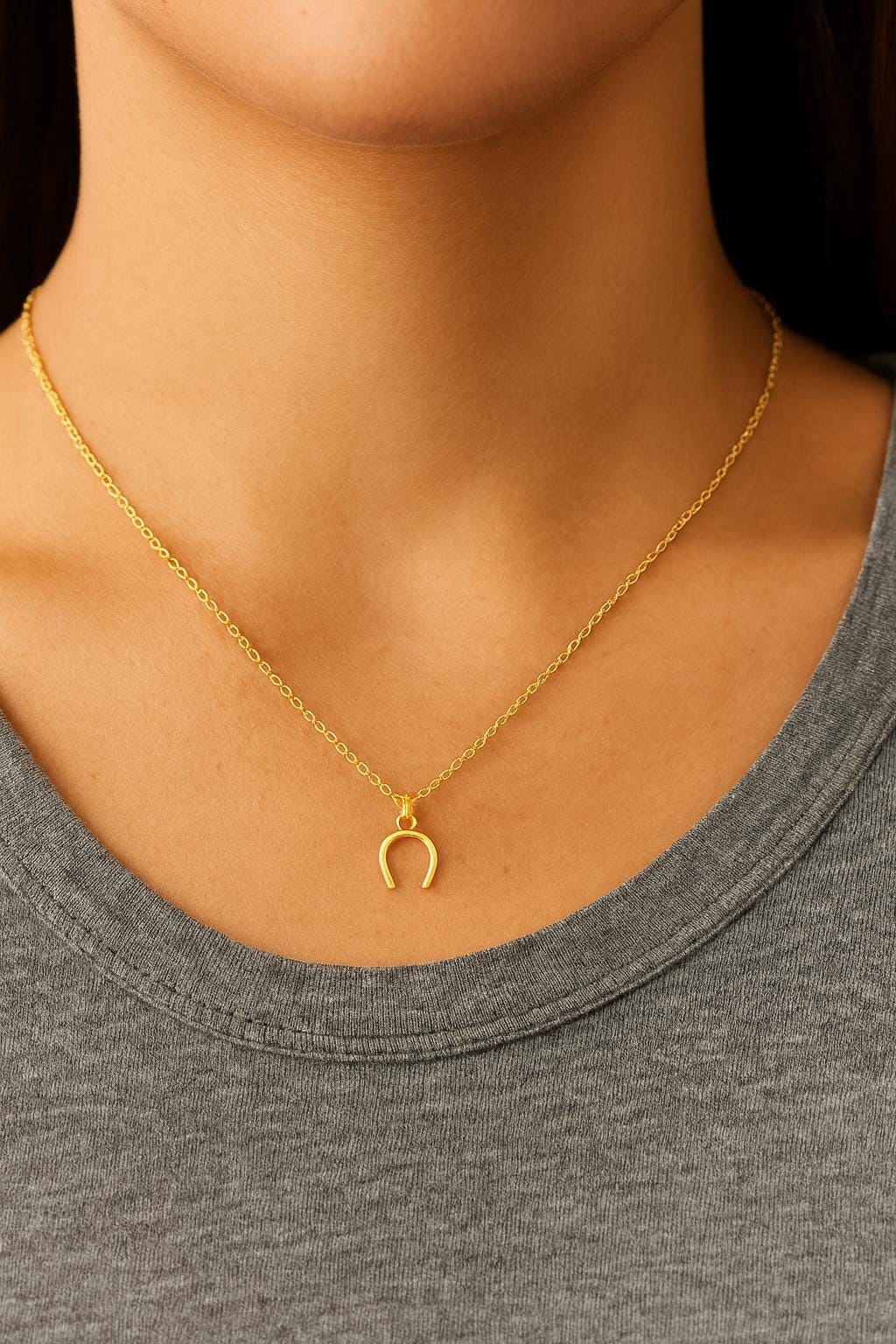 Gold necklace with a horseshoe pendant worn by a person in a gray shirt.