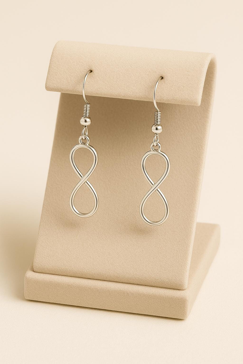 Silver infinity loop earrings on a beige earring stand.