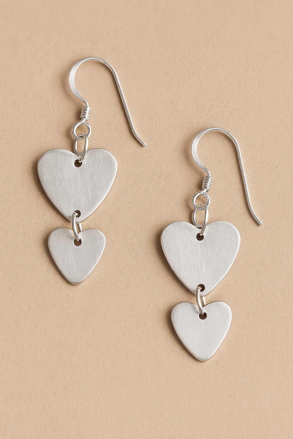 Silver heart-shaped earrings on a beige background