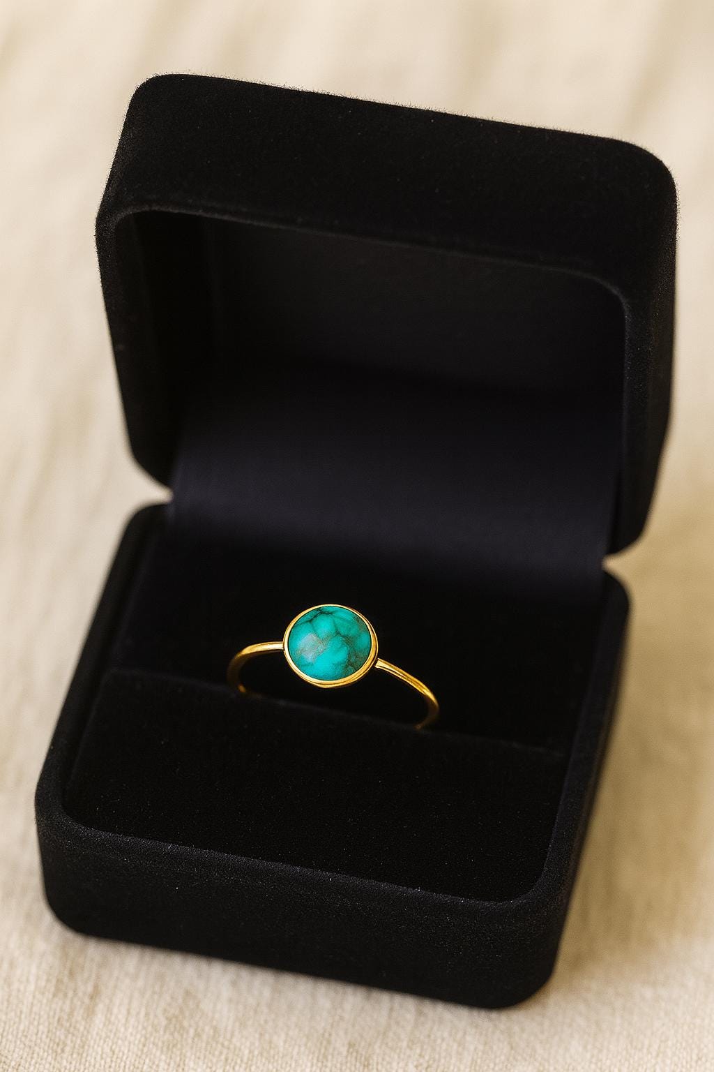 Gold ring with a green gemstone in a black jewelry box on a beige fabric background