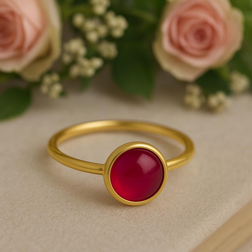 Gold ring with a red ruby gemstone on a beige surface with pink roses in the background