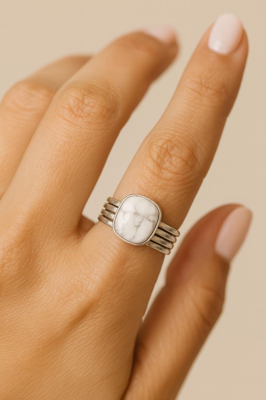 Hand wearing a silver ring with a white stone on a beige background