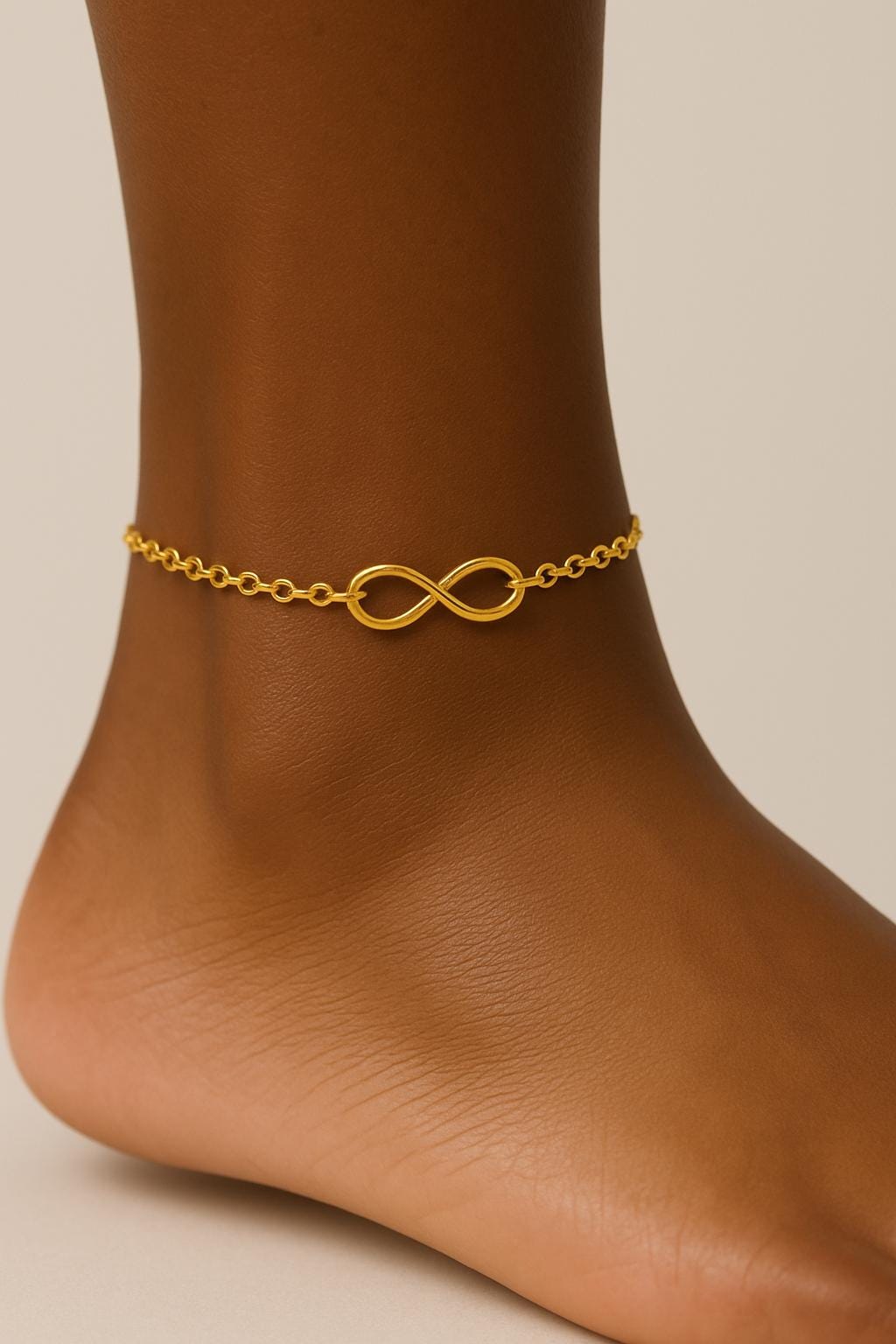 Gold anklet with infinity symbol on a person's ankle against a neutral background