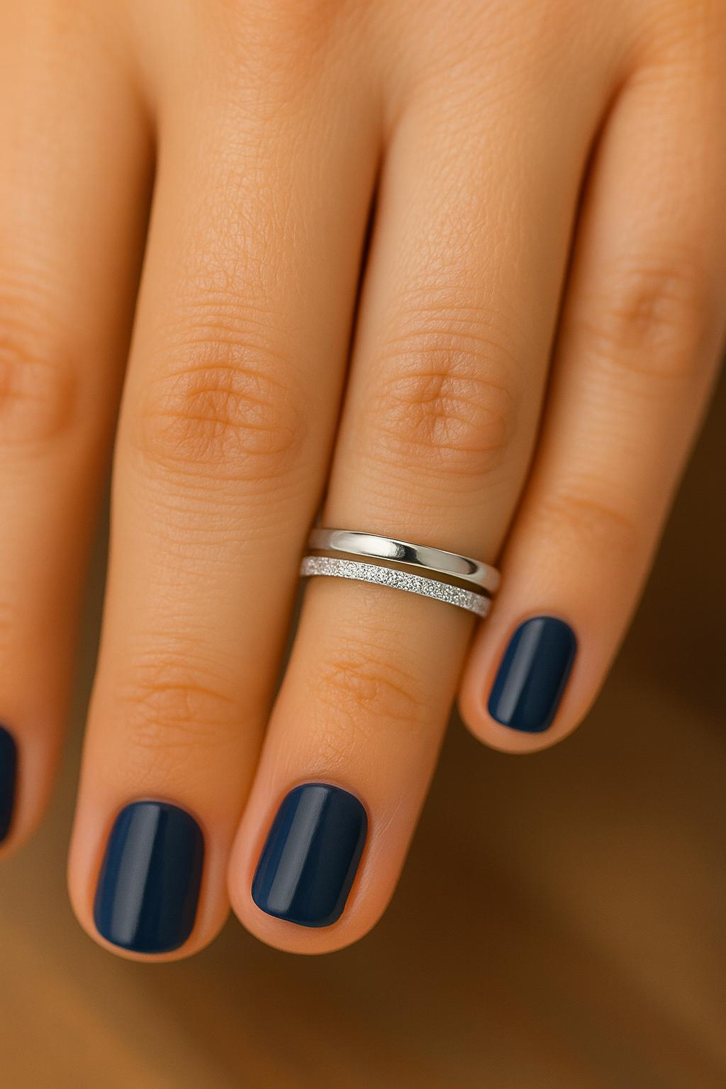 Hand with blue nail polish wearing a silver ring on a neutral background