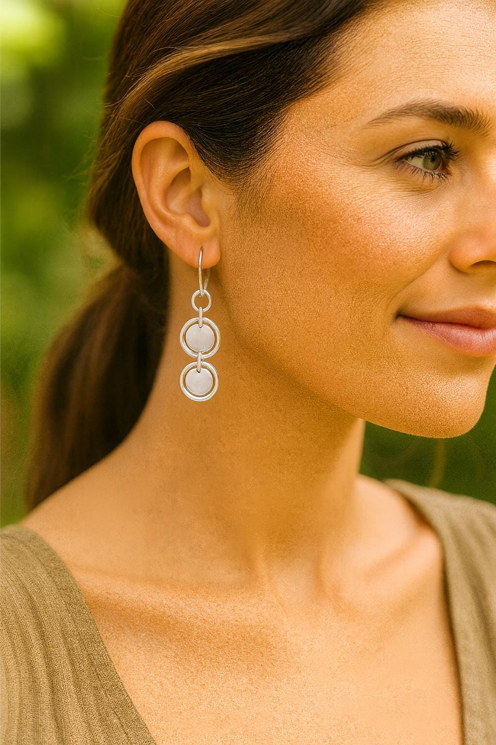Close-up of a woman wearing silver earrings with a blurred green background
