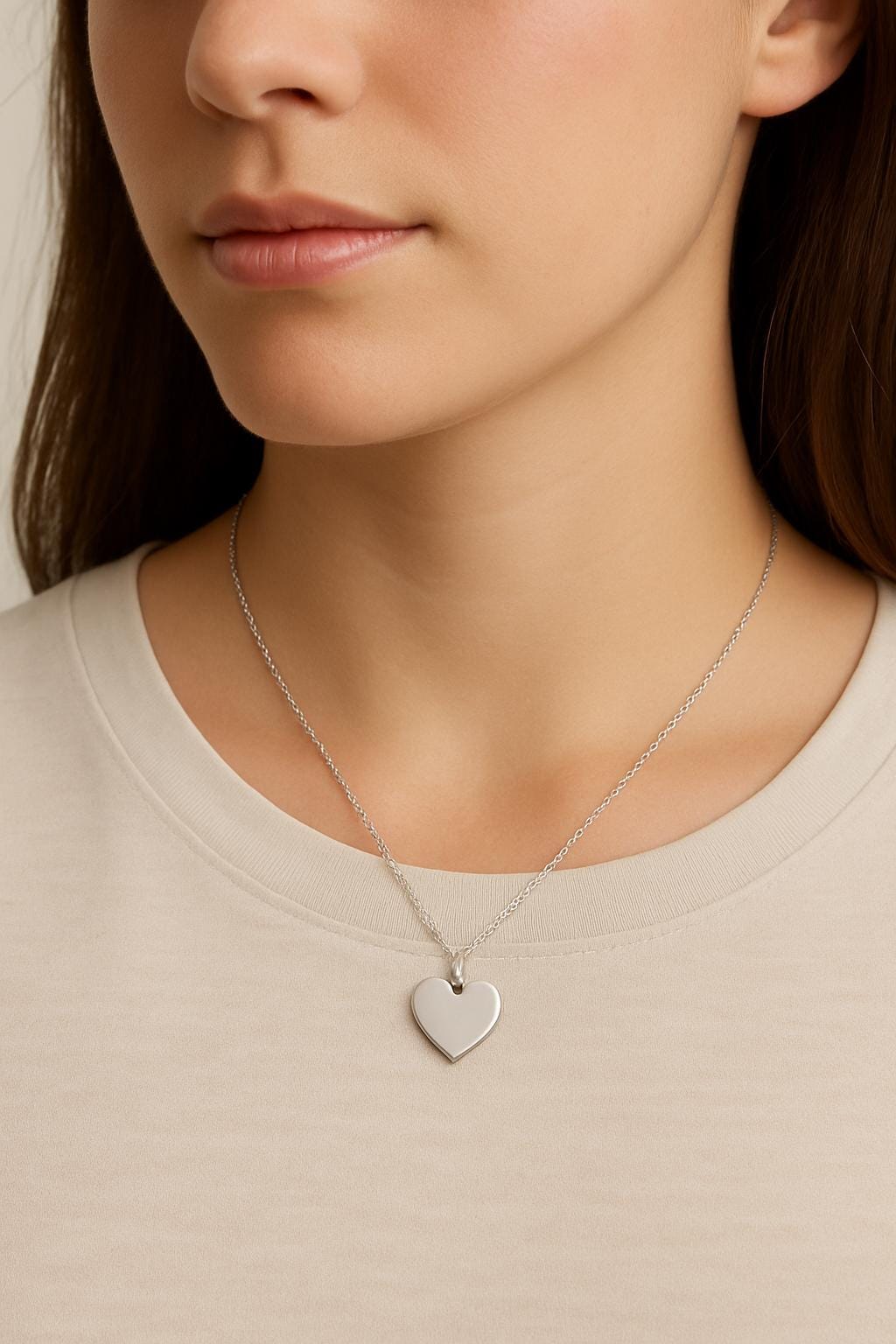 Close-up of a person wearing a silver heart-shaped necklace on a plain background