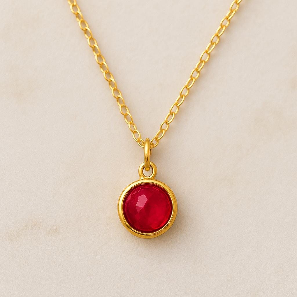 Gold necklace with a red gemstone pendant on a beige background