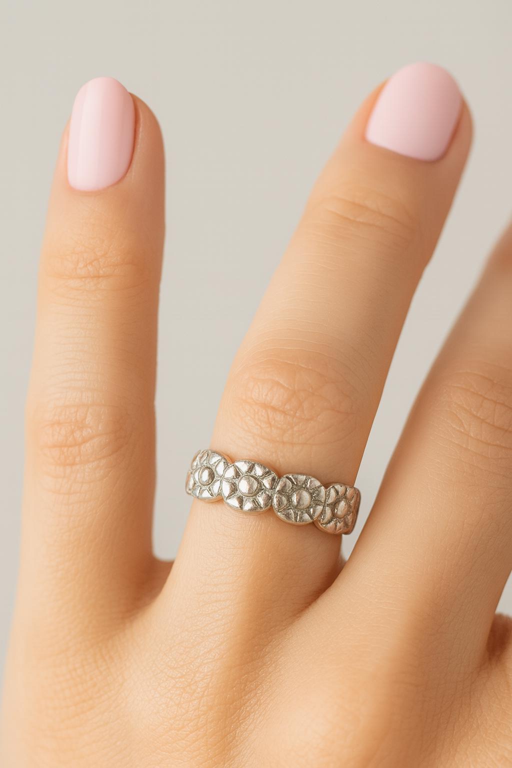 Silver flower ring on a finger with pink nail polish against a neutral background