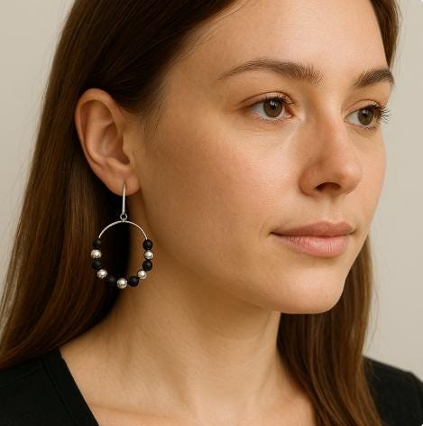 Woman wearing a hoop earring with black and silver beads on a neutral background