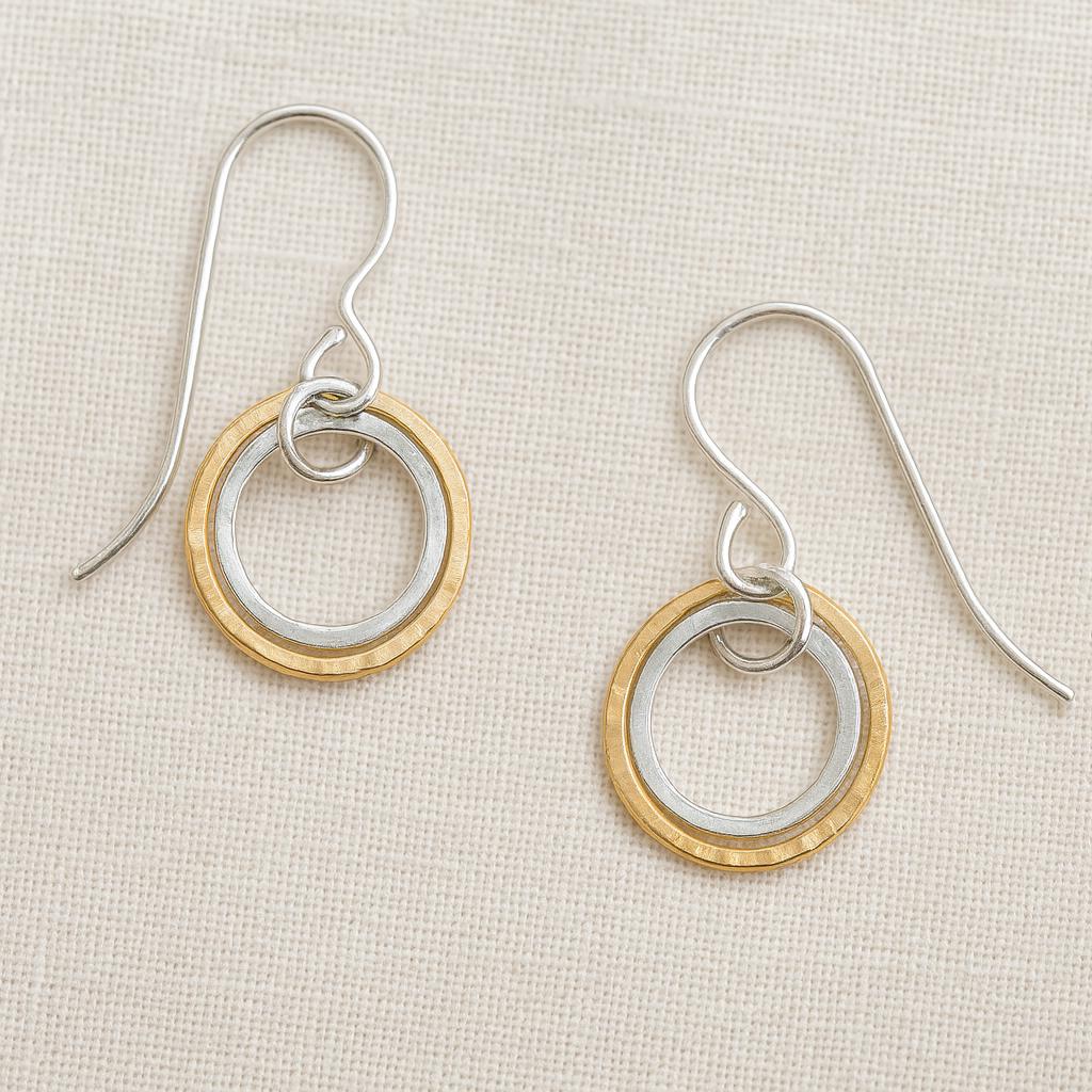 Pair of earrings with gold and silver circular designs on a beige fabric background
