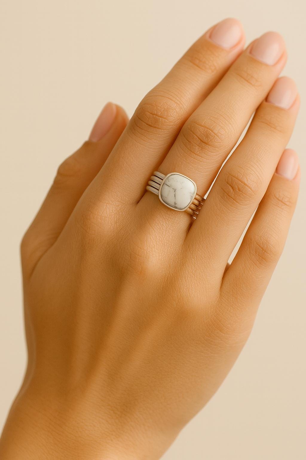 Hand wearing a silver ring with a stone on a beige background