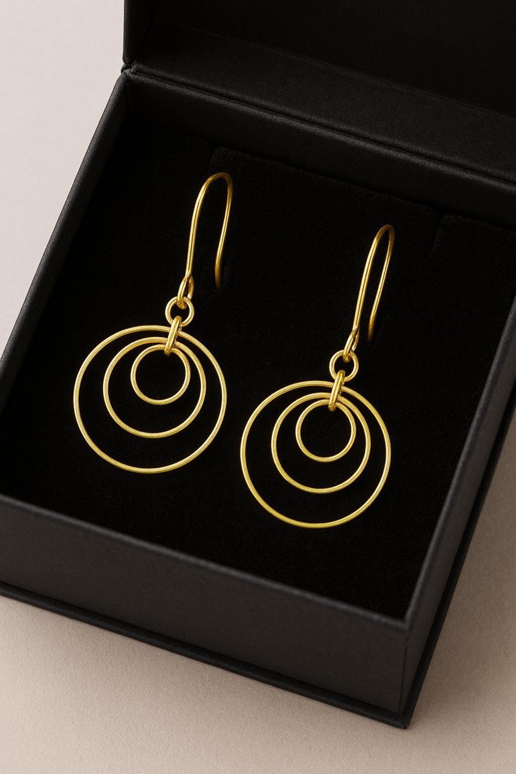 Gold Brass Dangle earrings on a textured surface with a black box in the background