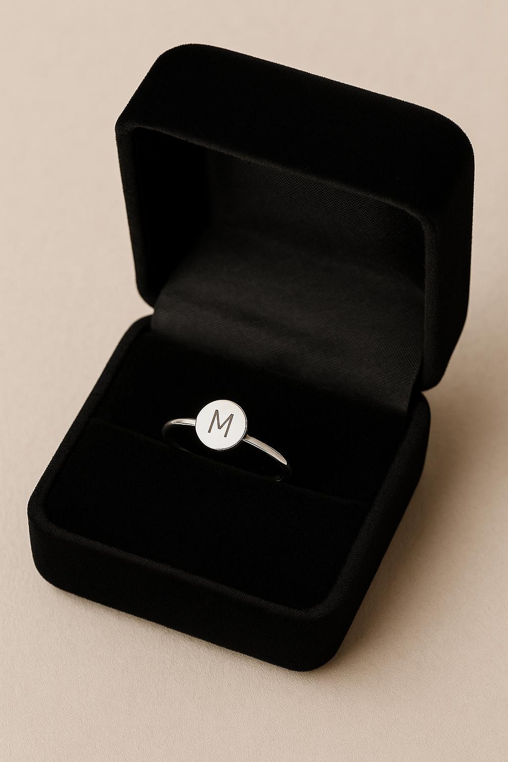 Silver ring with a circular emblem in an open black velvet box on a beige background