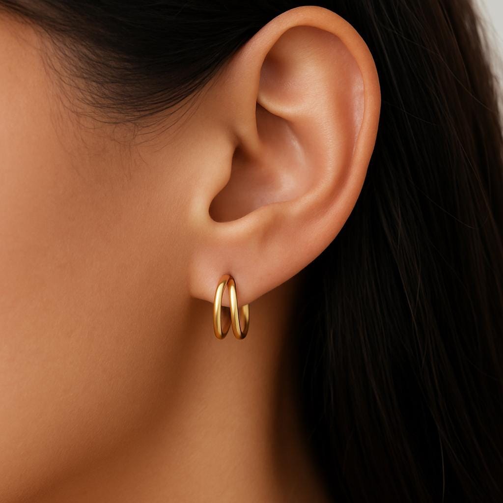 Close-up of an ear wearing a gold hoop earring with dark hair in the background