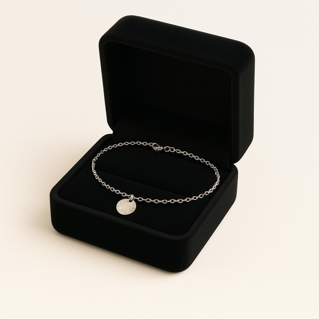 Silver bracelet with a round charm in an open black jewelry box on a light beige background
