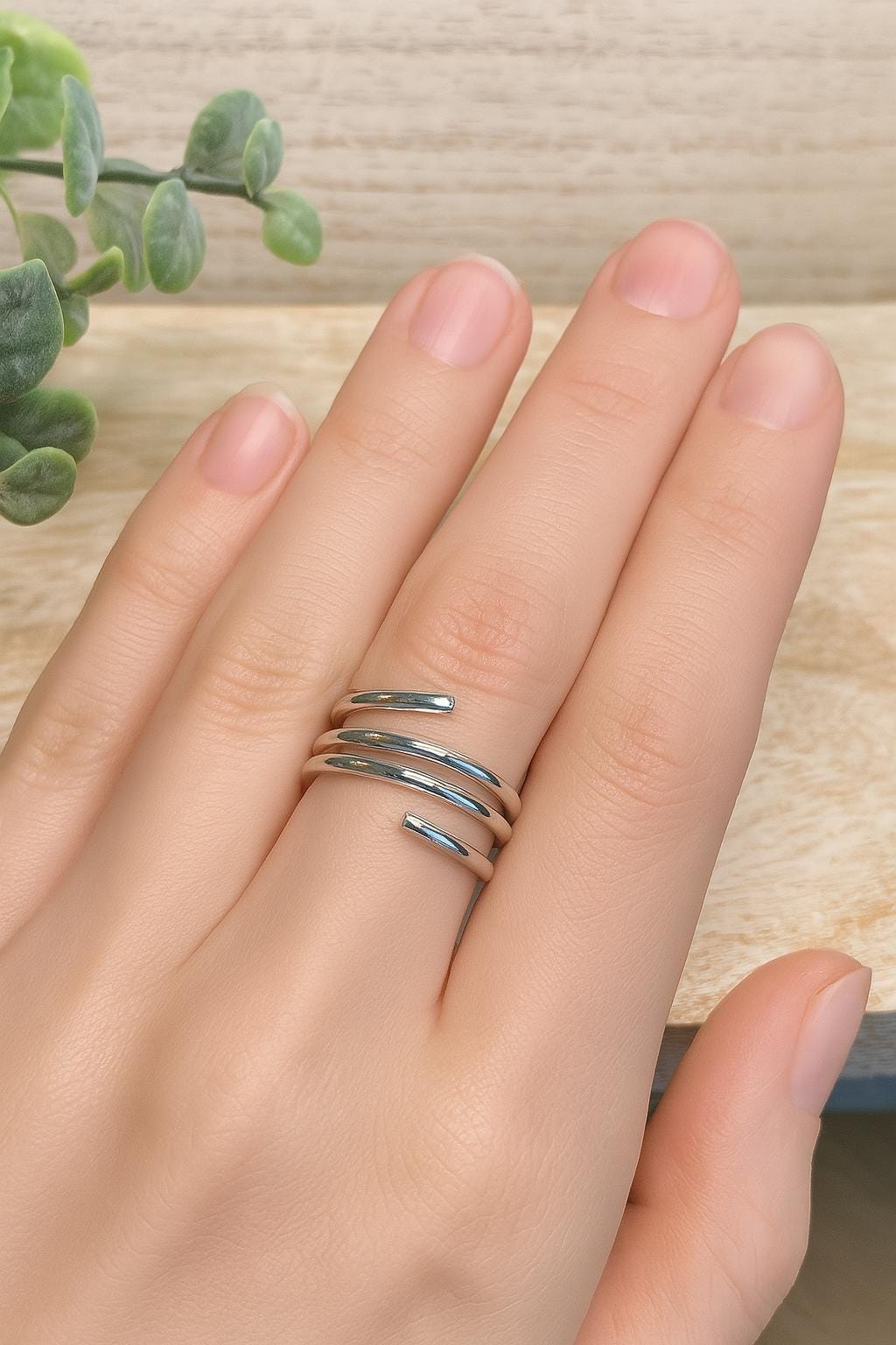Hand wearing a silver ring on a wooden surface with a plant in the background