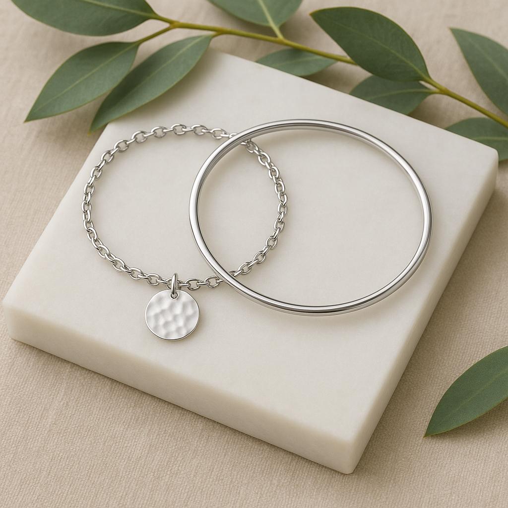 Two silver bracelets on a white stone surface with green leaves in the background