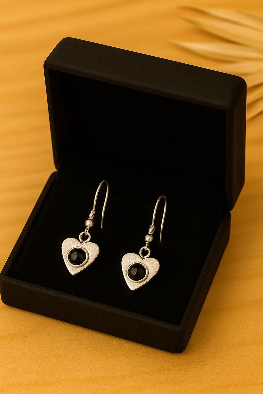 Heart-shaped earrings with a central gemstone in a black jewelry box on a wooden surface