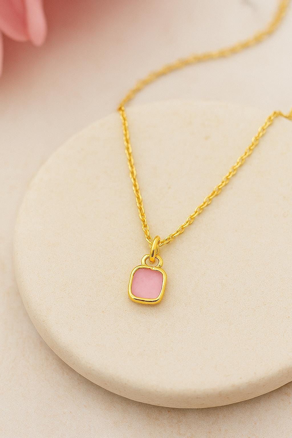 Gold necklace with a pink pendant on a beige surface