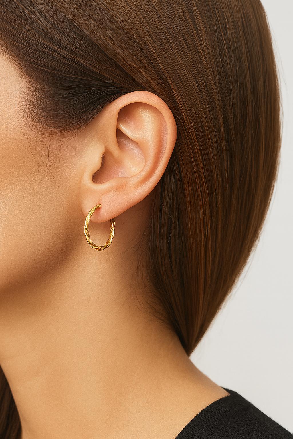 Close-up of a person wearing a gold hoop earring with a neutral background