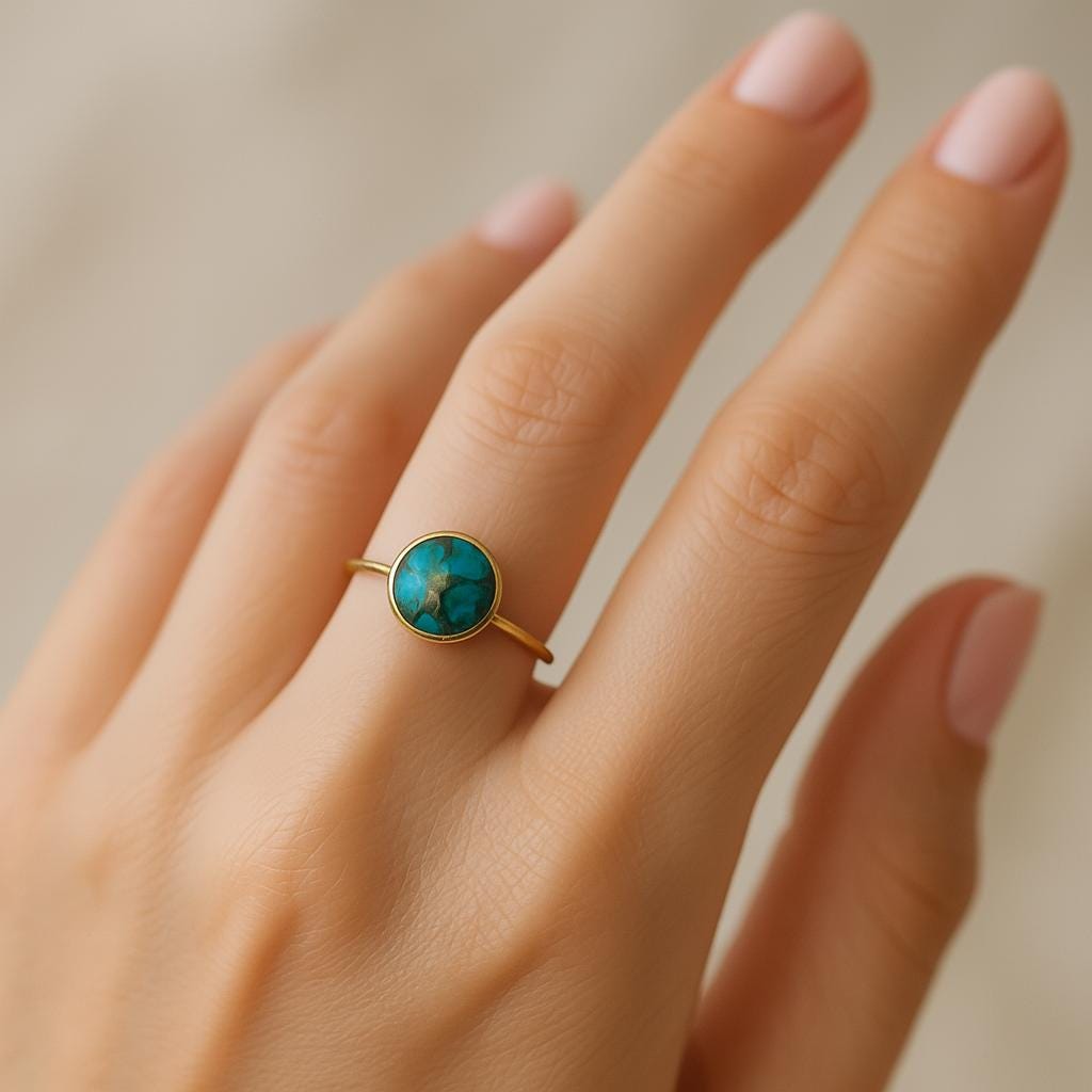 Gold ring with a green gemstone on a hand against a neutral background