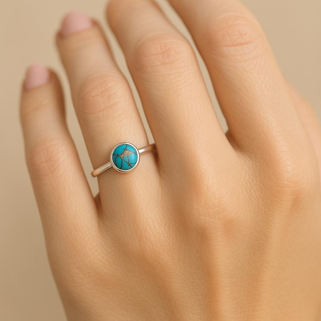 Hand wearing a ring with a turquoise stone on a beige background