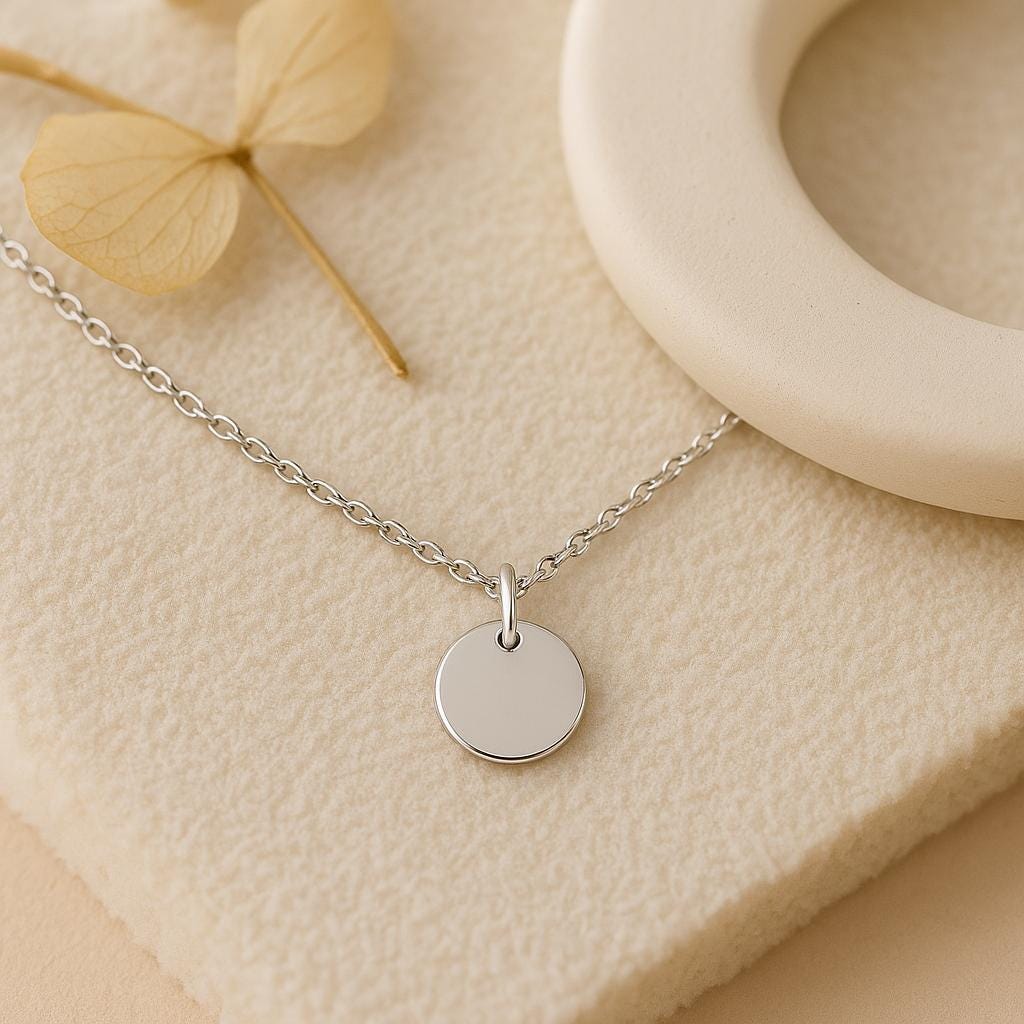 Silver necklace with a round pendant on a beige surface with dried leaves and a wooden ring.