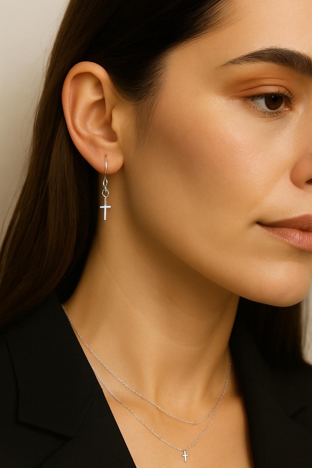Close-up of a woman wearing silver cross earrings and necklaces against a neutral background