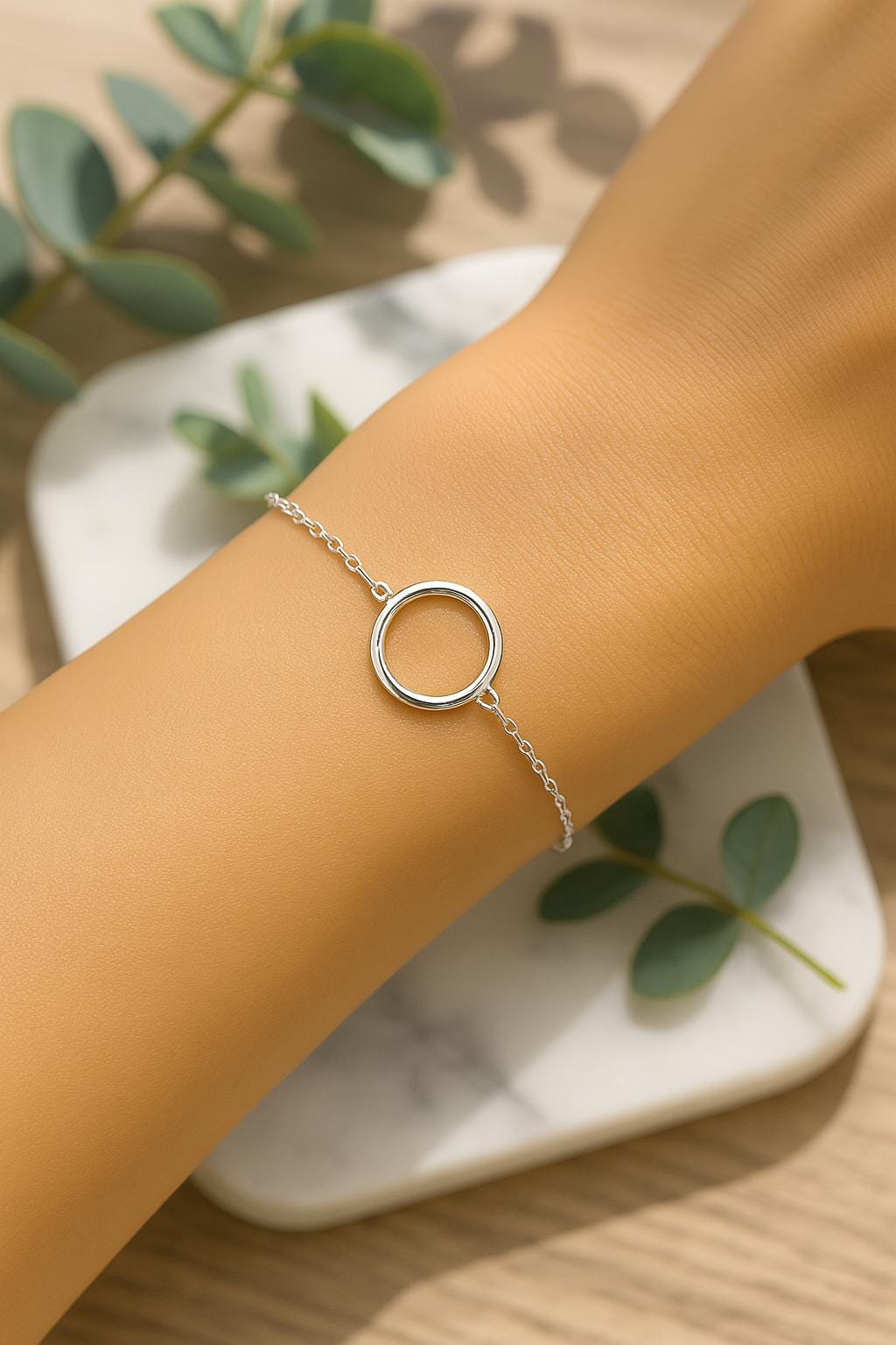 Silver bracelet with a circular design on a wrist, with green leaves in the background