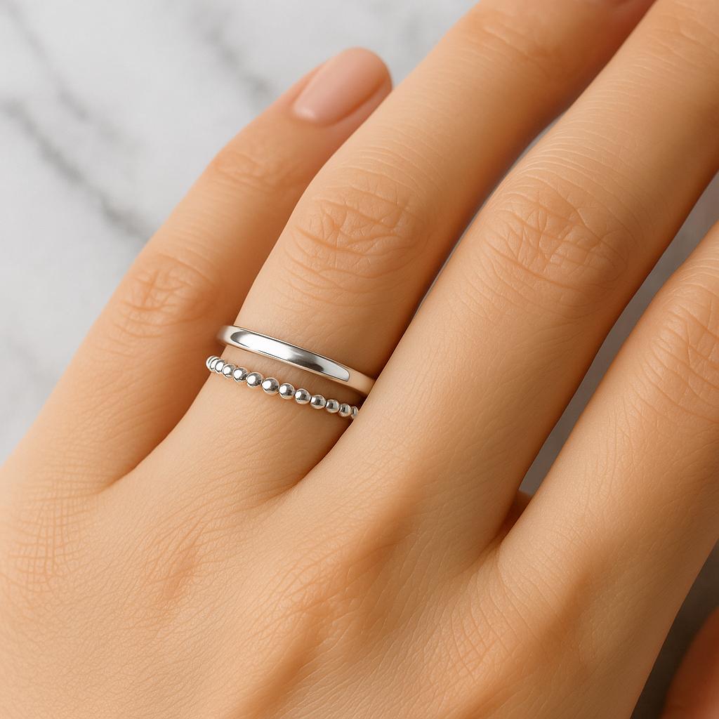 Silver ring with beaded design on a person's finger against a neutral background