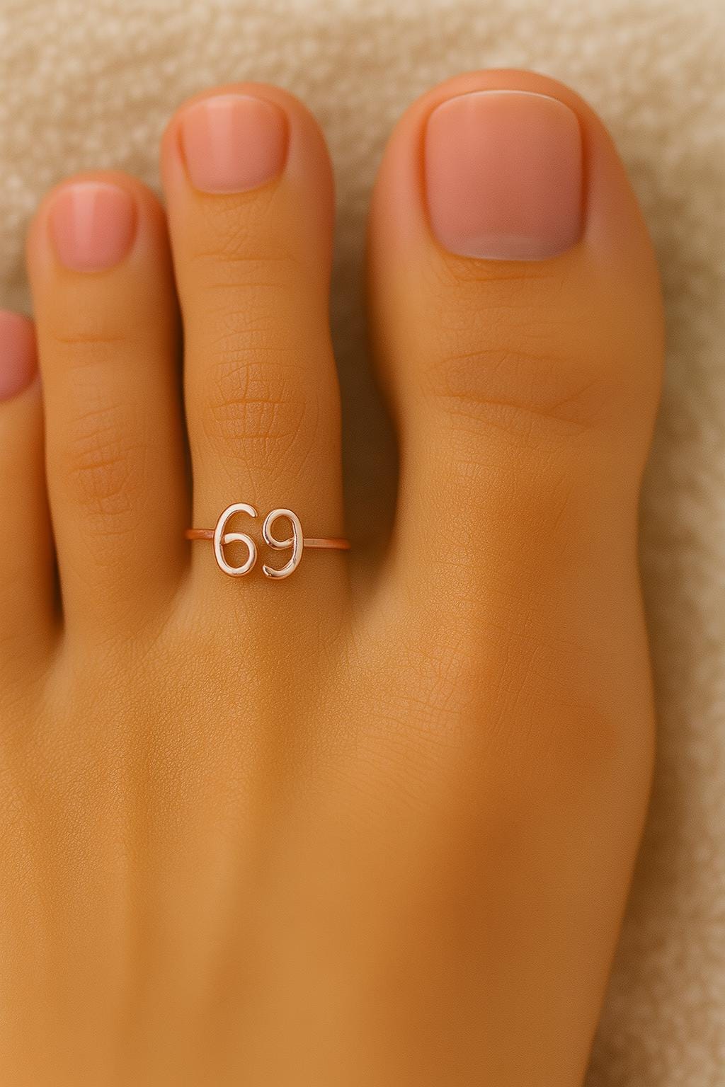 Toe ring with the number '69' on a foot against a beige background