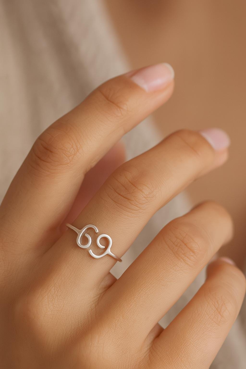 Silver ring with a unique design on a person's finger against a neutral background