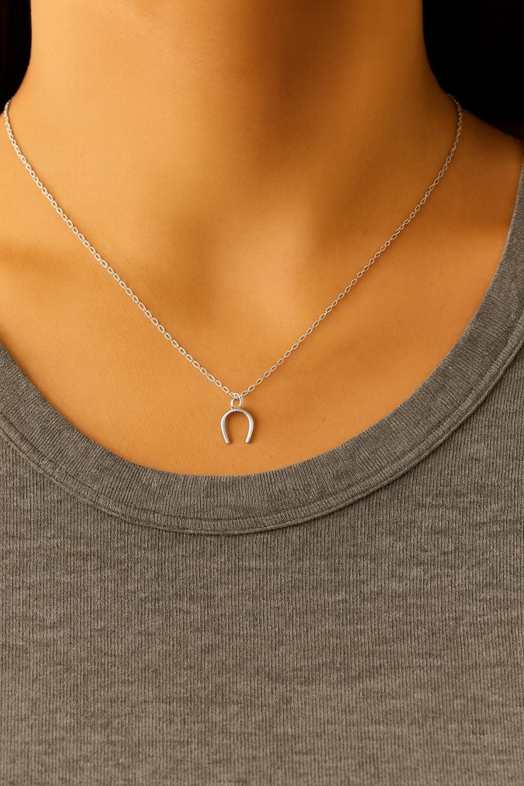 Silver necklace with a horseshoe pendant on a mannequin wearing a gray top.