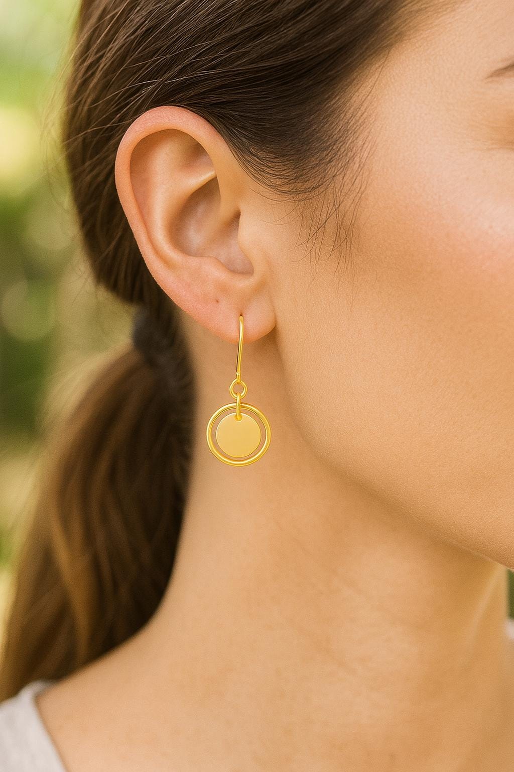 Close-up of a person wearing a gold earring with a blurred natural background