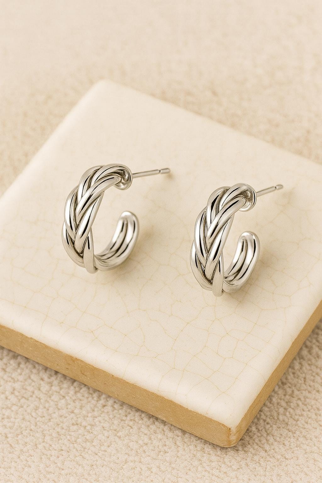 Pair of silver hoop earrings on a beige surface