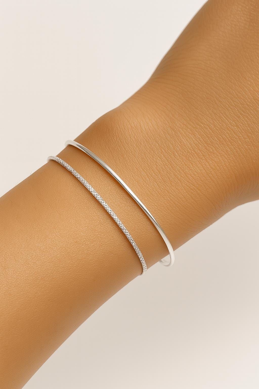 Silver bracelet on a wrist against a neutral background