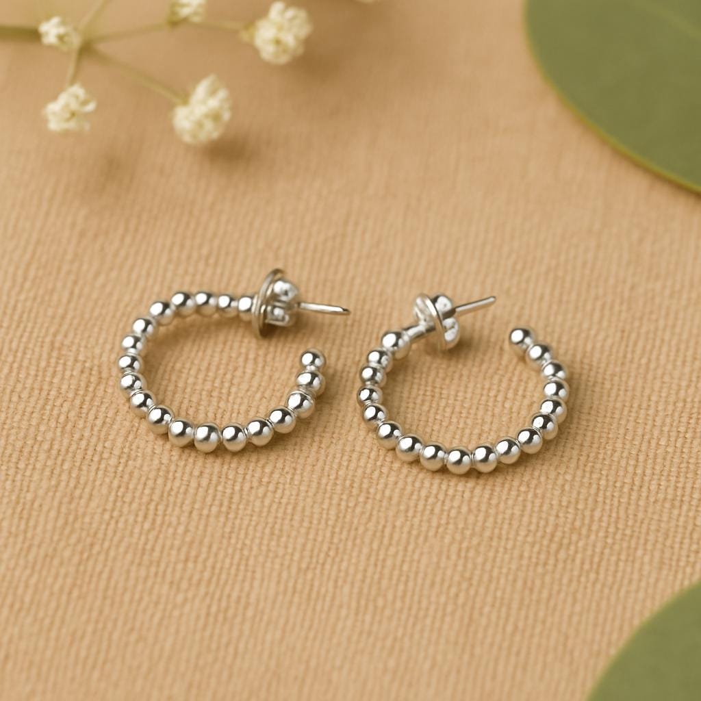 Silver hoop earrings on a beige surface with small white flowers and green leaves.