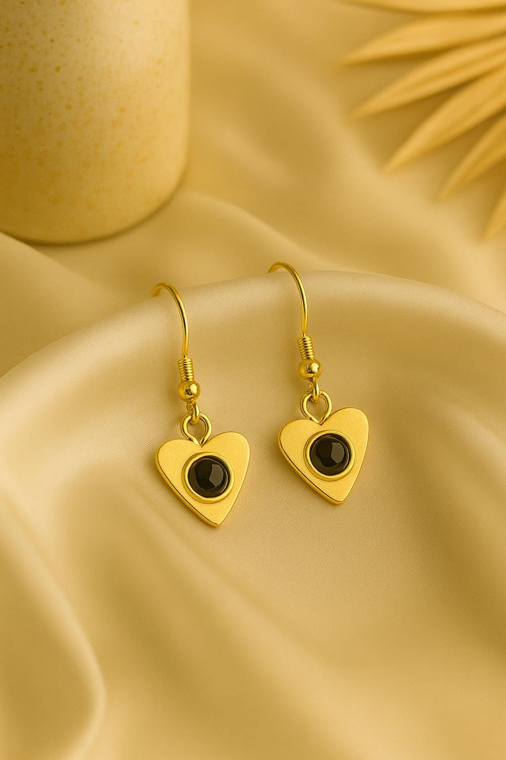 Gold heart-shaped earrings with black centers on a beige fabric background