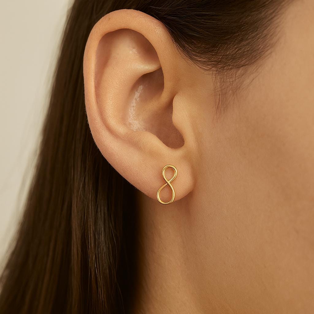 Gold infinity symbol earring worn by a person with dark hair.
