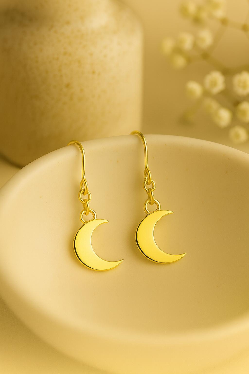 Gold crescent moon earrings on a beige plate with a soft background