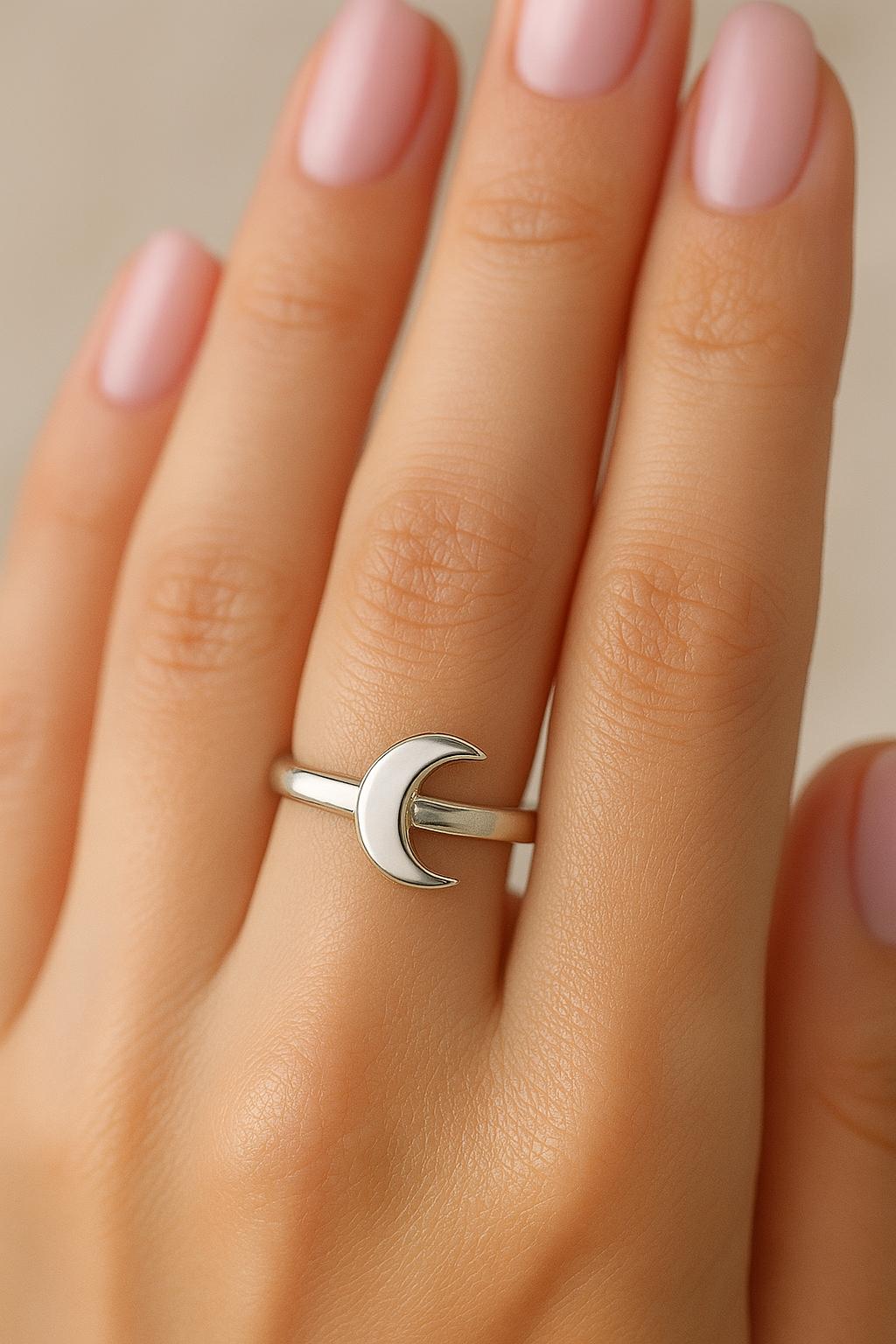 Silver ring with a moon design on a hand with pink nail polish.