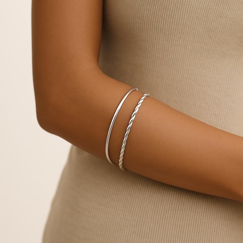 Silver bracelets on a person's wrist against a beige background