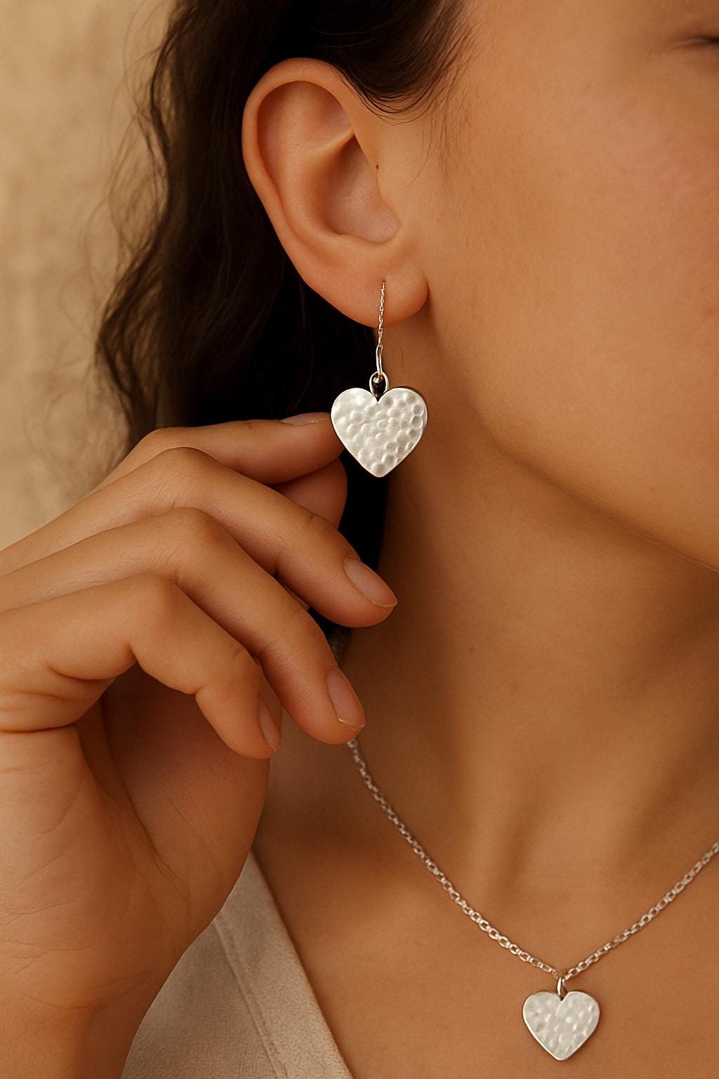 Close-up of a person wearing silver heart-shaped earrings and a necklace.