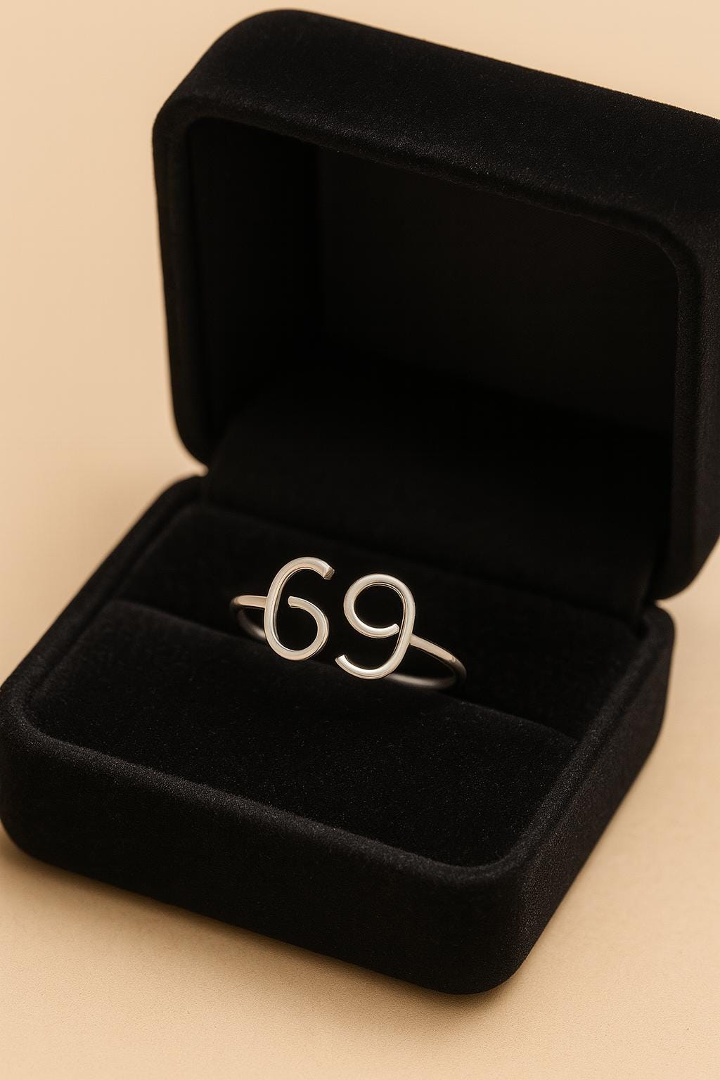 Silver ring with the number '69' in a black jewelry box on a beige background