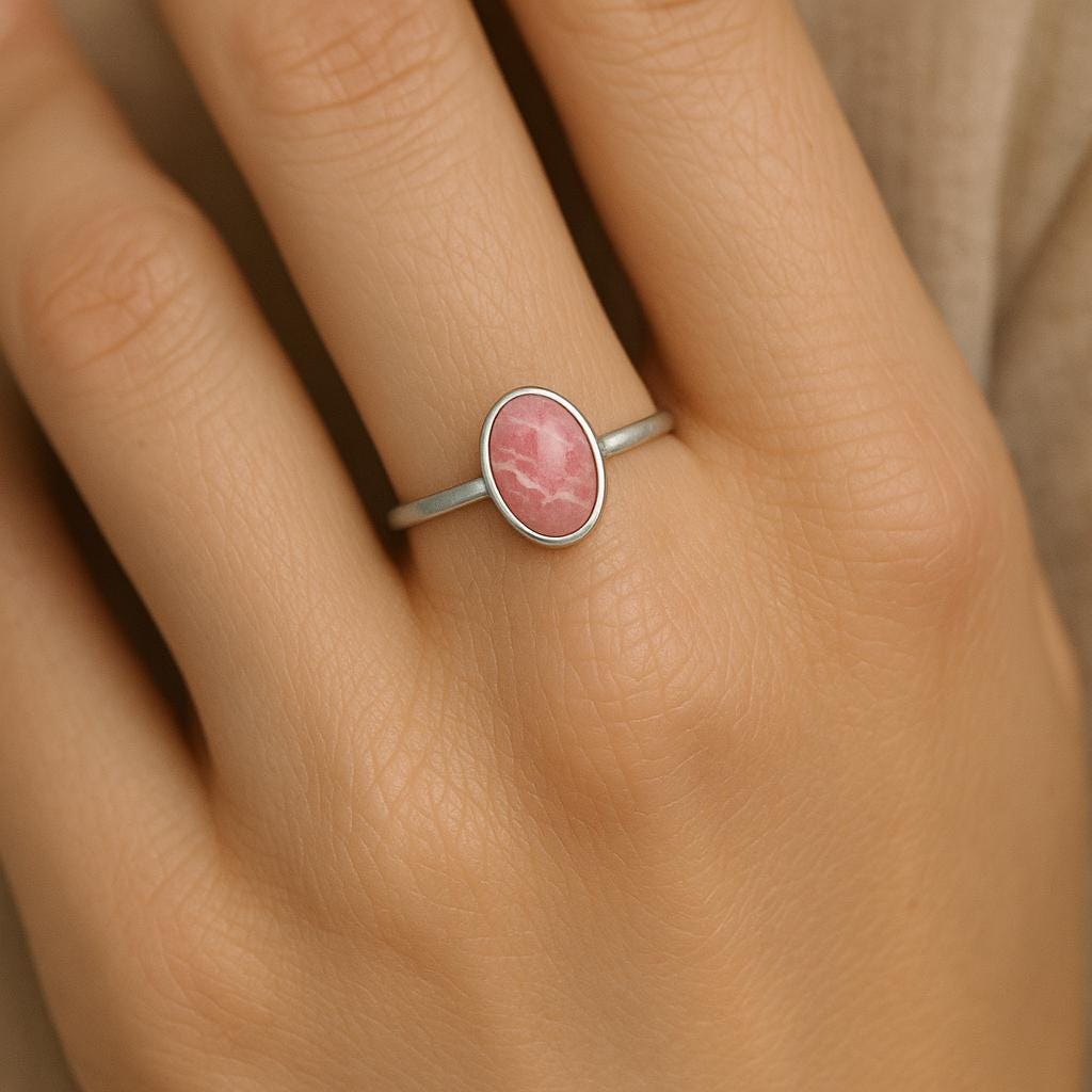 Pink gemstone ring on a person's finger against a neutral background
