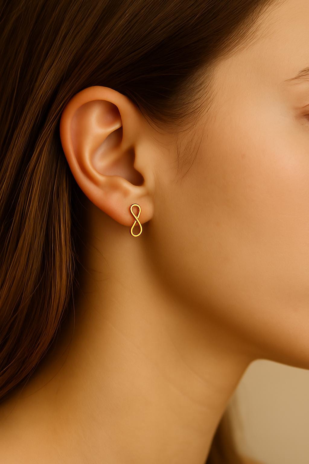 Close-up of an ear wearing a gold infinity symbol earring with a blurred background