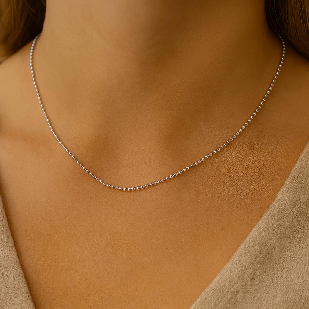Silver necklace on a person's neck with a neutral background