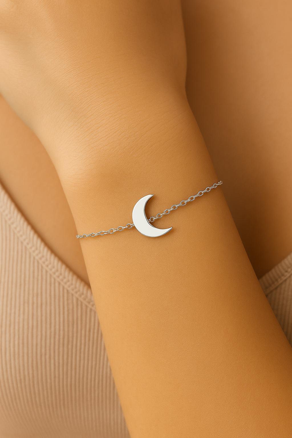 Bracelet with a moon charm on a wrist against a beige background