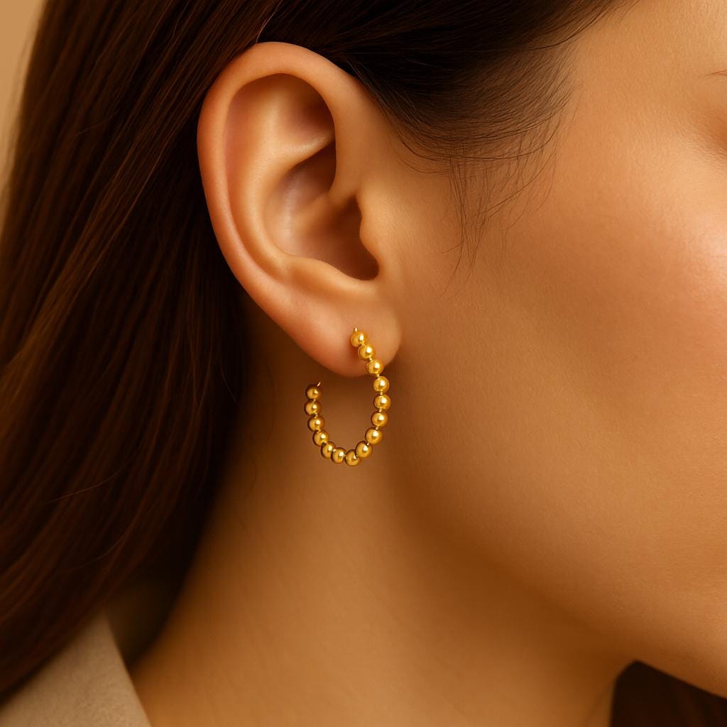 Close-up of an ear wearing a gold beaded hoop earring with a neutral background